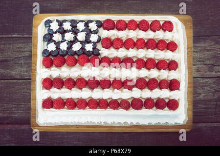 Patriotic, red white and blue, American flag cake, decorated with fresh blueberries and raspberries. Top view against rustic wooden background. Stock Photo