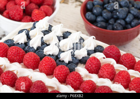 Patriotic, red white and blue, American flag cake. Fresh blueberries and raspberries in bowls in the background. Stock Photo