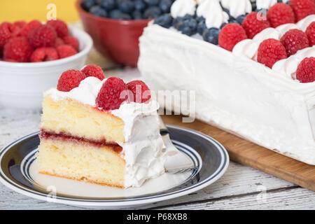 A slice of patriotic, red white and blue, American flag cake. The cake with fresh blueberries and raspberries in the background. Stock Photo