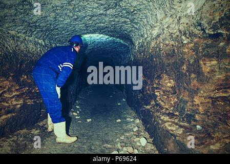 Dry sandstone tunnel, man worker in protective suite in underground. Mysterious dungeon tunnel with walls made inorange sandstone rock Stock Photo