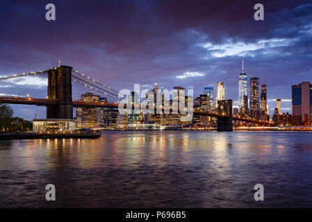 Brooklyn Bridge and illuminated Lower Manhattan skyscrapers at dusk with the East River. Manhattan, New York City, USA