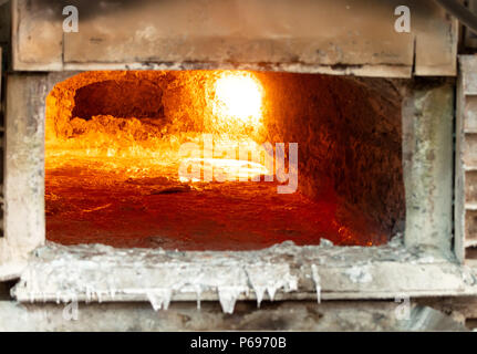 looking inside an aluminum melting furnace, in a foundry, with liquid metal and the oxidize dross layer on it Stock Photo