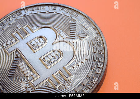 Chocolate product in the form of physical bitcoin lies on an orange plastic background. Model of the crypto currency in the edible form . Stock Photo