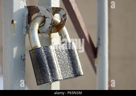A large gray padlock hangs on a metal gate . Stock Photo