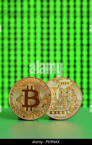 Two gold bitcoins lie on the green surface on the background of the display, which shows the process of mining the crypto currency . Stock Photo