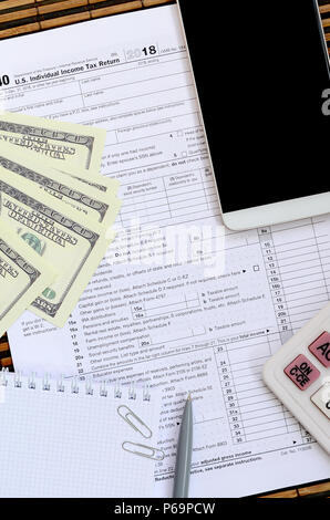 Composition of items lying on the 1040 tax form. Dollar bills, pen, calculator, smartphone, paper clip and notepad. The time to pay taxes . Stock Photo