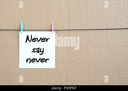 Never say never. Note is written on a white sticker that hangs with a clothespin on a rope on a background of brown cardboard . Stock Photo