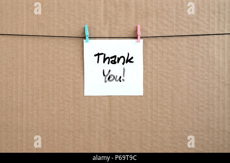 Thank you! Note is written on a white sticker that hangs with a clothespin on a rope on a background of brown cardboard . Stock Photo