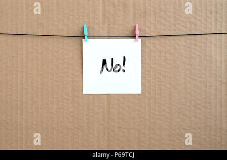 No! Note is written on a white sticker that hangs with a clothespin on a rope on a background of brown cardboard . Stock Photo