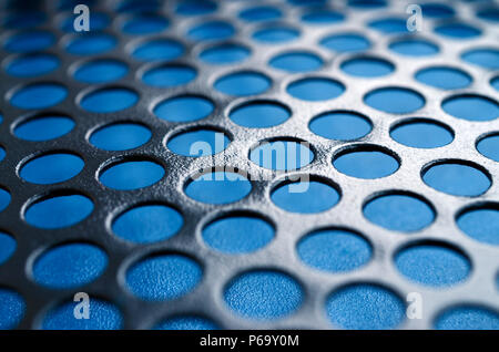 Black metal computer case panel mesh with holes on blue background. Abstract close up image . Stock Photo
