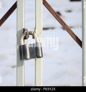 A large gray padlock hangs on a metal gate . Stock Photo
