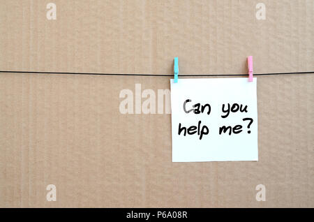 Can you help me? Note is written on a white sticker that hangs with a clothespin on a rope on a background of brown cardboard . Stock Photo