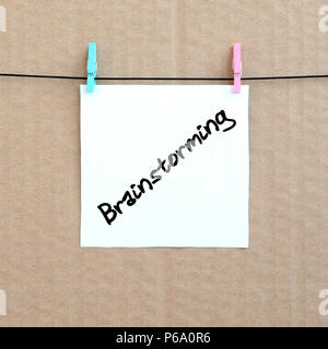 Brainstorming. Note is written on a white sticker that hangs with a clothespin on a rope on a background of brown cardboard . Stock Photo