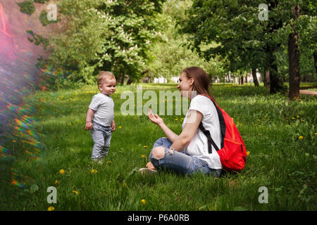 Family. Son and mother outdoors. Pregnant girl with backpack sitting on lawn. Little boy is standing next to her Stock Photo