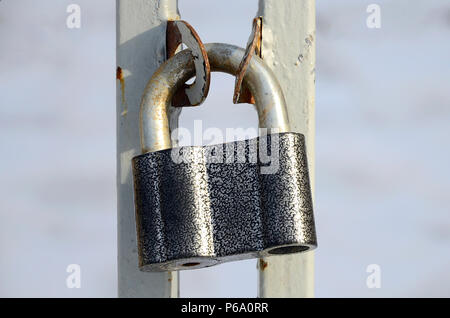 A large gray padlock hangs on a metal gate . Stock Photo