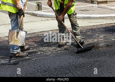 Workers using asphalt paver tools during road construction. Stock Photo