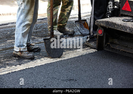 Workers using asphalt paver tools during road construction. Stock Photo