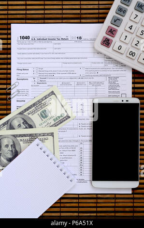 Composition of items lying on the 1040 tax form. Dollar bills, calculator, smartphone, paper clip and notepad. The time to pay taxes . Stock Photo