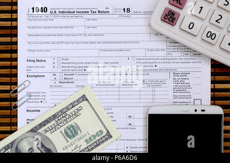 Composition of items lying on the 1040 tax form. Dollar bills, calculator, smartphone, paper clip and notepad. The time to pay taxes . Stock Photo