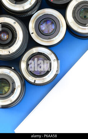 Several photographic lenses and white notebook lie on a bright blue background. Space for text . Stock Photo