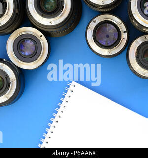 Several photographic lenses and white notebook lie on a bright blue background. Space for text . Stock Photo