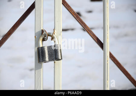 A large gray padlock hangs on a metal gate . Stock Photo