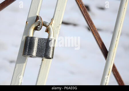 A large gray padlock hangs on a metal gate . Stock Photo