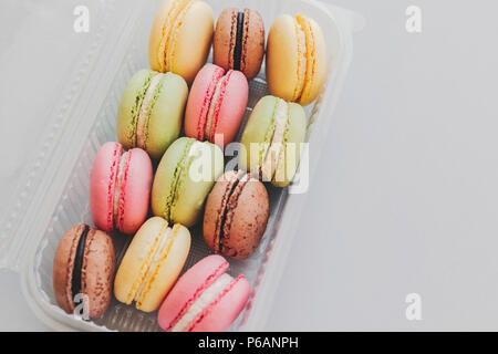 delicious colorful macaroons in plastic box on trendy pastel gray paper. tasty pink, yellow, green and brown macaroons. space for text. candy for part Stock Photo