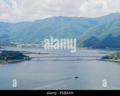 Scenery of Lake Kawaguchi, the biggest lake of Fuji five lakes, with a ferry boat and an overwater bridge crossing the lake and mt Kurodake on the background, famous tourist destination in Japan Stock Photo