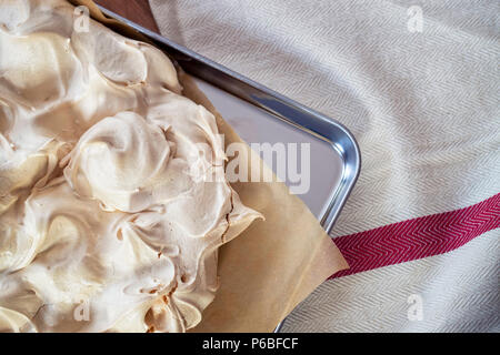 Cooking the meringue base for a Pavlova dessert. Fresh meringue, with crisp golden top, on baking parchment and a stainless steel baking tray. Overhea Stock Photo