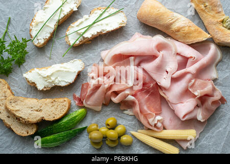 Cold appetizer. Cold cuts. Different snacks on a white crumpled paper, ham, bread, vegetables, from above. Stock Photo