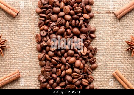 Coffee beans geometric vertical organized layout with symmetrical cinnamon sticks in the corners and badges stars on a sackcloth background. Copyspace Stock Photo