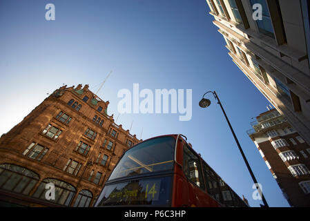 Low angle shot of the architcture in Knightsbridge with a sign to the London underground and a red London bus passing by Stock Photo