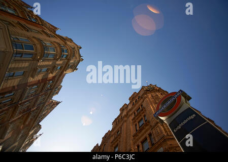 Low angle shot of the architcture in Knightsbridge with a sign to the London underground and a red London bus passing by Stock Photo