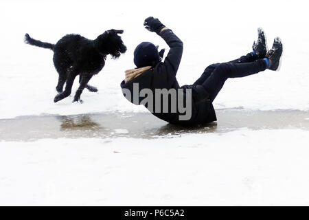 Berlin, Germany, boy slips over an ice surface accompanied by his dog on the pants Stock Photo