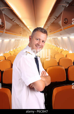 joyful and smiling captain of plane in uniform stands in the cabin Stock Photo