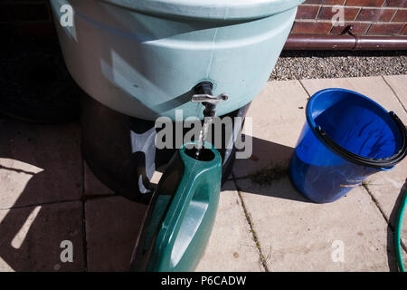 Filling watering can with rainwater from waterbutt to water plants during drought Stock Photo