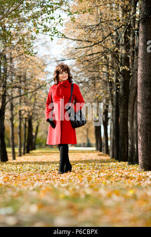 The  mature beautiful woman in red topcoat,  outdoor in park, autumnal day Stock Photo