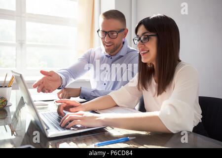 Two Happy Businesspeople Using Laptop At Workplace Stock Photo