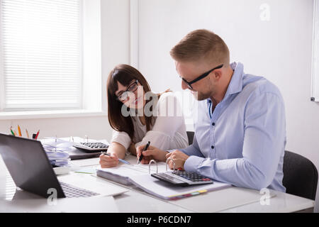 Two Young Businesspeople Calculating Invoice With Calculator Stock Photo