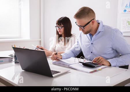 Two Young Businesspeople Calculating Invoice With Calculator Stock Photo
