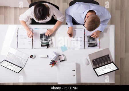 Two Young Businesspeople Calculating Invoice With Calculator Stock Photo