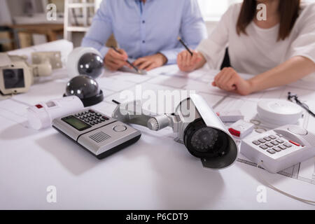 Various Security Equipments In Front Of Two Architects Planning Project On Blueprint Stock Photo