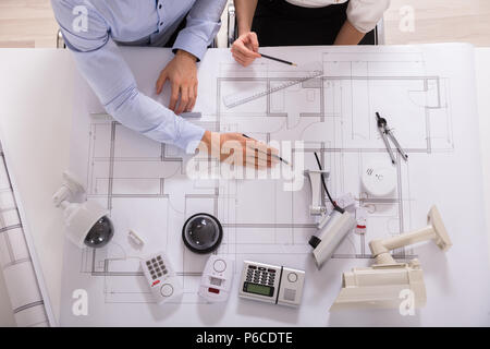 High Angle View Of Two Architects Working On Blueprint With Various Security Equipments Stock Photo
