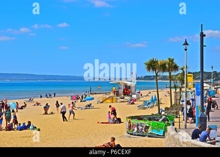 Hot sunny weather & the palm trees give this beach scene a tropical feel as people enjoy the beach next to  Bournemouth Pier in the Summer time Stock Photo