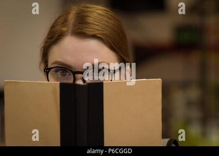 Woman with spectacles hiding face behind book Stock Photo