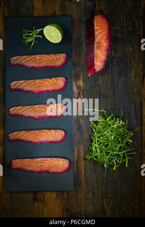 Sliced salmon fillet, salted with beetroot juice, served on whole wheat with salad leaves, sea salt and pepper over metal surface. Top view. Stock Photo