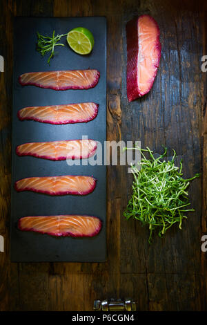 Sliced salmon fillet, salted with beetroot juice, served on whole wheat with salad leaves, sea salt and pepper over metal surface. Top view. Stock Photo