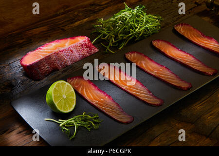 Sliced salmon fillet, salted with beetroot juice, served on whole wheat with salad leaves, sea salt and pepper over metal surface. Top view. Stock Photo