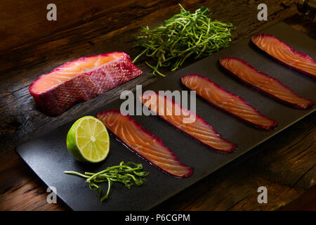 Sliced salmon fillet, salted with beetroot juice, served on whole wheat with salad leaves, sea salt and pepper over metal surface. Top view. Stock Photo